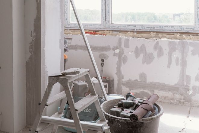 Leerer Raum während der Renovierung mit Leiter und Eimer vor dem Fenster